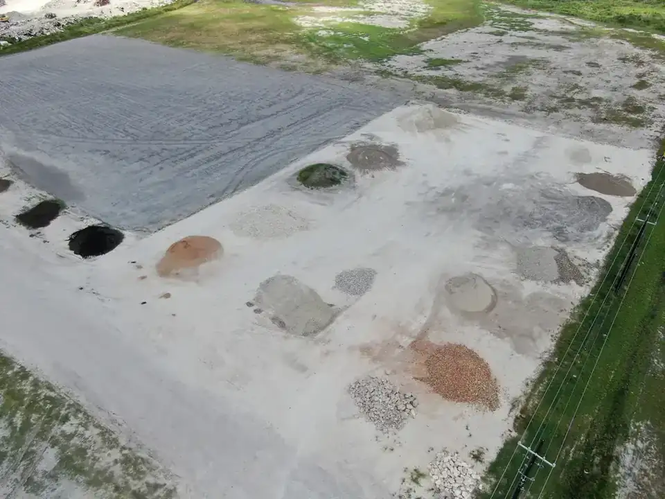 Aerial view straight down on the Aaron Concrete materials yard, showing a dozen separated stockpiles of crushed base, sand, riprap and topsoil
