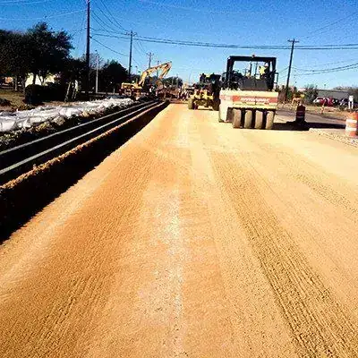 A prepared roadway subgrade with a curb line run and a grader working behind it