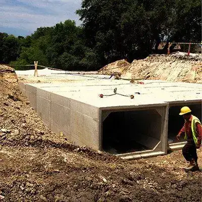 A finished precast box culvert and headwall, a worker walking out of the trench