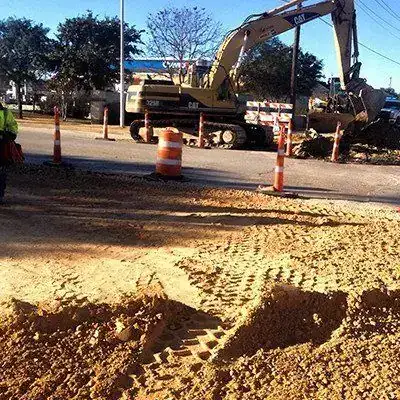 A CAT excavator working in a street with road base spread and traffic control barrels out